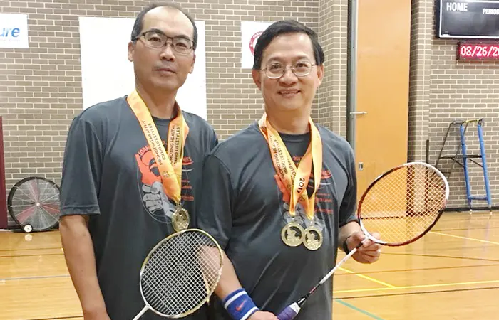 Senior badminton players holding rackets and medals indoors