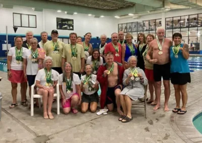 Senior swimmers posing with medals at indoor pool