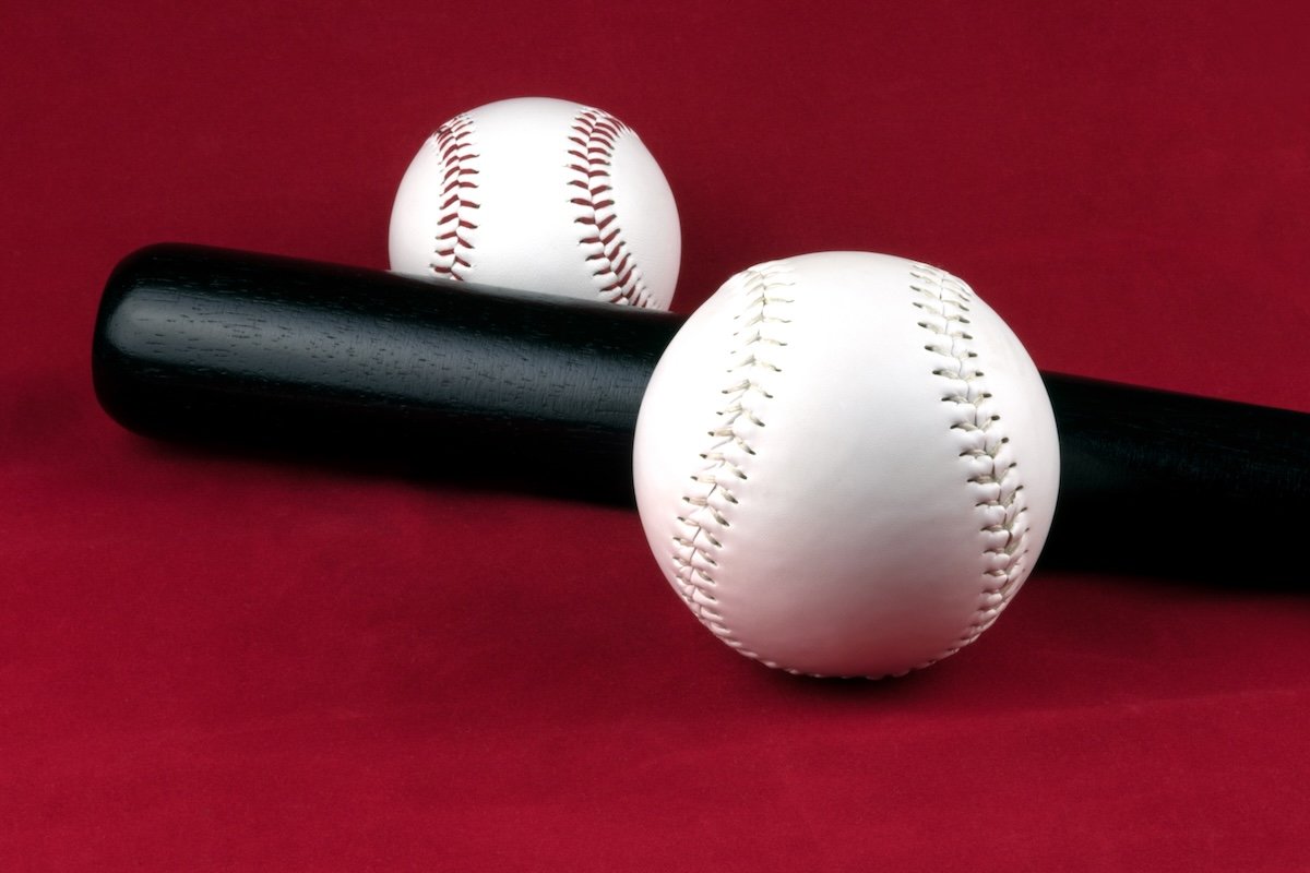 Large and small softballs and black bat on a red background