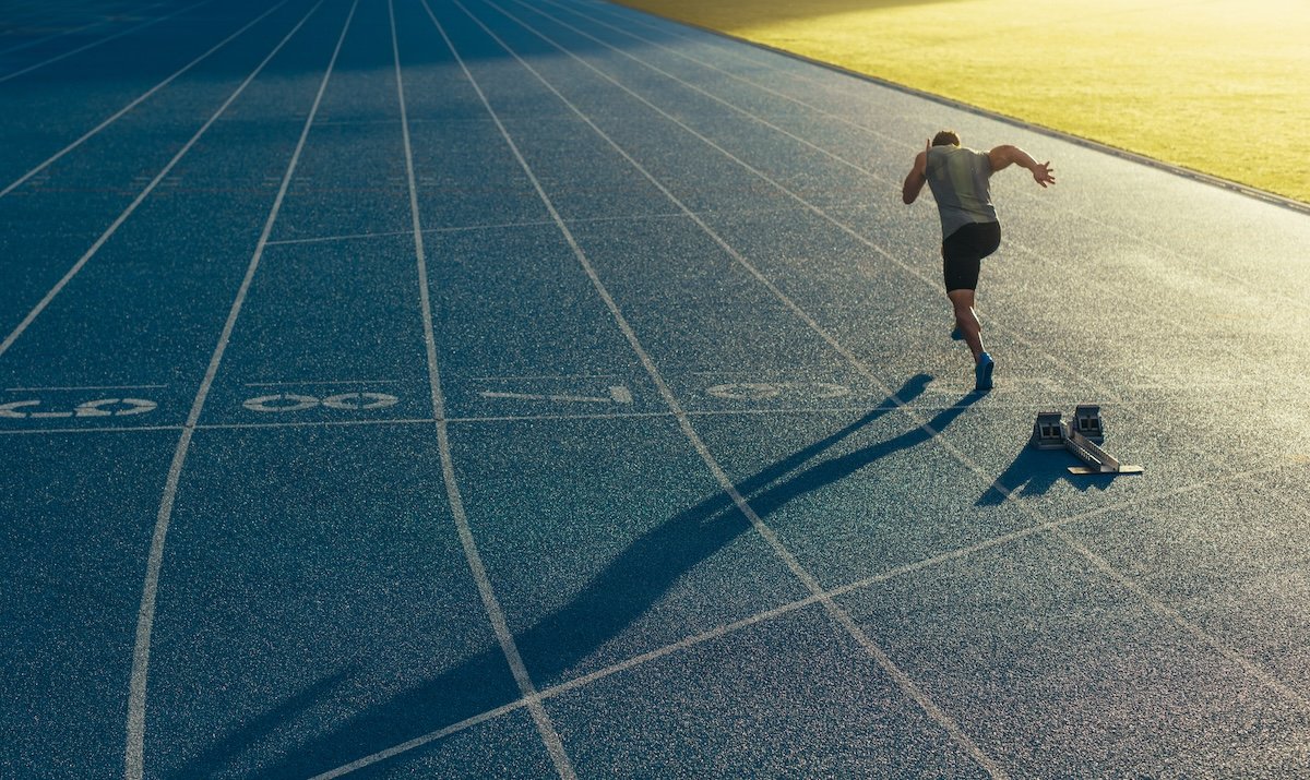 Idaho Senior Games National Games 2027 Athlete running on an all-weather running track alone. Runner sprinting on a blue rubberized running track starting off using a starting block.